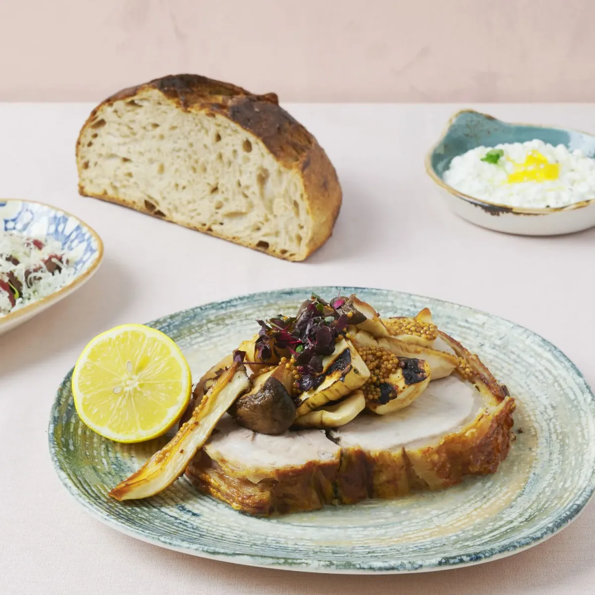 Lækker frokost serveret med sprødt brød, hytteost og en hovedret med svampe og citron